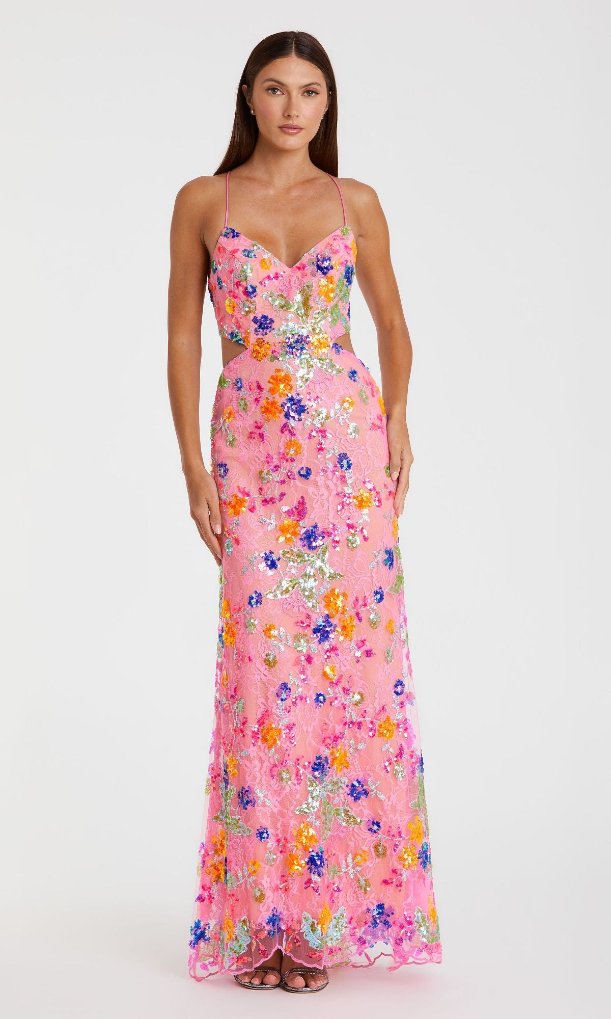 A woman stands against a white background wearing the Mac Duggal 68067 Sequin-Print Pink Formal Dress, a long pink gown with spaghetti straps and colorful floral patterns and sequins.